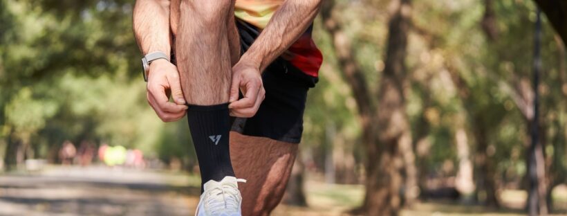 Löpare drar upp en svart sportsocka över benet i en park